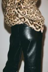 Pantalón de tejido revestido con acabado efecto cuero, de corte recto y tiro medio. Presenta cierre frontal con cremallera, pretina con botón oculto, bolsillos laterales al bies y costura horizontal visible sobre las rodillas.