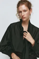 Camisa de corte holgado confeccionada en tejido satinado con mezcla de lyocell. Presenta cuello redondo con escote en pico y lazada frontal integrada. Cuenta con mangas largas abullonadas terminadas en puños anchos y bajo recto.