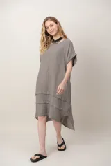 Vestido midi de lino color beige, de corte holgado y silueta acampanada. Cuenta con cuello redondo, mangas cortas amplias, bolsillos laterales y detalles de recortes horizontales en la falda con terminación asimétrica más larga en la parte trasera.