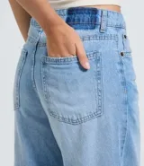 Pantalón de jean modelo wide leg en color azul medio, con cintura baja y corte holgado. Presenta roturas decorativas en las rodillas, bolsillos funcionales, cierre frontal con botón y cremallera, y trabillas para cinturón.