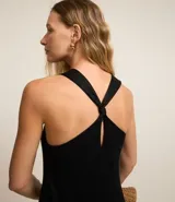 Vestido midi de corte evasé confeccionado en tejido piquet color negro. Presenta un diseño sin mangas con escote en V, breteles anchos cruzados en la espalda con detalle de nudo y falda con recortes de volados en la parte inferior.