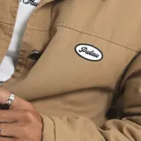 Campera estilo carpenter color beige con cuello de pana en contraste color marrón. Presenta cierre frontal con botones metálicos, bolsillos frontales con solapa y parche bordado con logo en el pecho. El interior cuenta con forro acolchado.