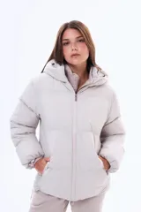 Campera puffer de corte holgado en color beige, con capucha integrada, cierre frontal completo y bolsillos laterales. Presenta un diseño acolchado con acabado mate y puños elásticos.
