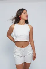 Top corto tipo halter de cuello a la base, confeccionado en gabardina de algodón. Presenta pinzas delanteras que aportan volumen, cierre lateral y detalle de abertura con botón en la espalda. Se caracteriza por sus costuras a contratono.