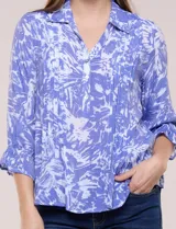 Blusa azul con estampado tipo pincelada en tonos blancos, cuello solapa con escote en V, media abotonadura frontal con botones nacarados, mangas tres cuartos con puños elásticos y diseño semi holgado.