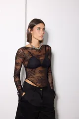 Remera de encaje negro con diseño asimétrico, manga larga y cuello redondo. Presenta un patrón floral y un corte ajustado al cuerpo.