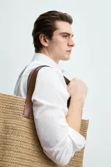 Bolso tipo shopper de acabado trenzado color tostado, con compartimento principal sin cierre, bolsillo plano interior y dos asas de mano de cuero sintético marrón.