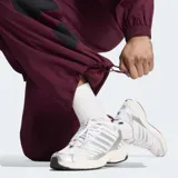 Pantalón deportivo Adidas Originals holgado de color bordó, con cintura elástica, tiro medio y detalles de tres tiras grandes negras en los laterales de las pantorrillas.
