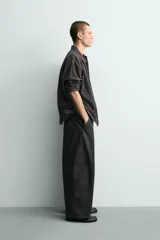 Pantalón de corte relajado confeccionado en tejido de algodón. Presenta cintura con trabillas laterales ajustables, bolsillos frontales y traseros, y un diseño distintivo de costuras laterales giradas que recorren la pernera.