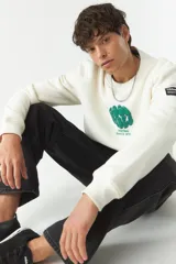 Buzo de felpa color crudo con cuello redondo y estampado frontal con el texto 'Good Vibes' y el logo de la marca Mistral. Tiene un parche con el logo de la marca en la manga izquierda.