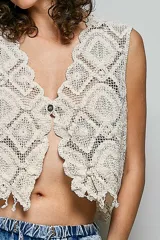 Chaleco de crochet color beige, de corte relajado, con cuello en V, ribete de flecos festoneados y cierre frontal de un botón.