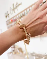 Pulsera elástica de cuentas doradas con dijes irregulares de acabado metálico brillante.