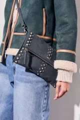 Cartera bandolera negra con tachas plateadas, confeccionada en gamuza vegana.