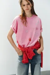 Camiseta oversize de algodón color rosado, con efecto lavado, cuello redondo y manga corta. Presenta aplicaciones de brillos con motivos de Hello Kitty y amigos.