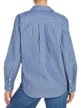 Camisa de manga larga a rayas verticales azules y blancas, con cuello inglés y corte amplio. Presenta detalles distintivos de la marca Tommy Hilfiger y logo bordado en el puño.