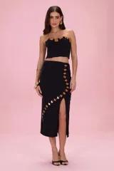 Falda midi negra de punto, con silueta ajustada, tajo lateral y detalle de apliques circulares de piedras en tonos marrones y negros que recorren el lateral de la prenda.