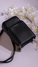 Cartera porta celular negra de cuero sintético con doble compartimento con cierre y correa larga regulable.