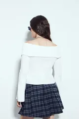 Top de punto acanalado negro, con diseño off-shoulder y escote amplio. Presenta mangas largas y cierre frontal completo con doble cursor, permitiendo ajustar la apertura superior e inferior.