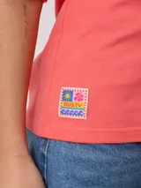 Remera color amarillo pastel con estampado de palmeras, flores de hibisco y texto 'California Ride the Tide Rusty Tribe'.