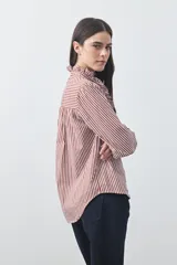 Camisa de manga larga a rayas verticales en tonos blanco y bordó, con cuello alto y detalle de volados frontales. Presenta puños con volados y un corte fluido.