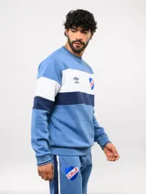 Buzo de cuello redondo confeccionado en felpa, con diseño de bloques de color en azul, rojo y blanco. Presenta el logo de Umbro y el escudo del Club Nacional de Football bordados en el frente.