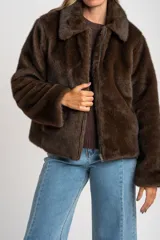 Abrigo de piel sintética en color marrón, con cuello clásico, cierre frontal con cremallera y mangas largas.