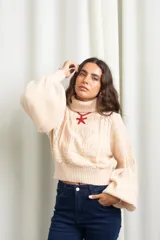 Polera de punto color manteca, con cuello alto, diseño de trenzas y flores en el frente, y mangas globo amplias.