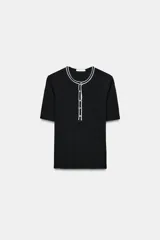 Camiseta de punto ajustada con cuello redondo y manga corta. Presenta detalles de vivos en color blanco a contraste en el cuello y la tapeta frontal, que cuenta con cierre de botones metálicos.