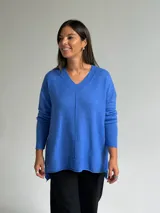 Sweater de tejido de punto color azul, con escote en V, manga larga con puños acanalados y diseño holgado con costura central vertical y ruedo asimétrico.