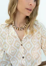 Camisa de fibrana de estilo clásico, con estampa ikat en tonos beige y blanco, cuello camisero, mangas largas y botones de coco en la parte frontal.