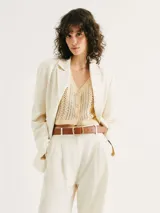 Chaleco de punto calado en color beige, con escote en V y cierre frontal con botones. Presenta un diseño sin mangas y corte recto.