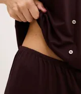 Pijama capri Lov confeccionado en poliéster y elastano, color marrón, compuesto por una blusa de manga corta con escote en V y botones frontales, y un pantalón capri con cintura elástica. Ambos detalles presentan aplicaciones de encaje.