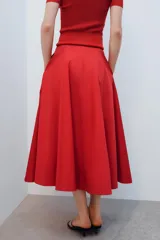 Falda midi de tiro alto y corte en A, color rojo, con bolsillos laterales ocultos y cierre lateral con cremallera.