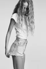 Short de jean negro desgastado, tiro alto, con roturas pronunciadas y terminación deshilachada en el bajo. Presenta cinco bolsillos y cierre frontal con botón metálico.