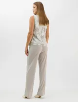 Conjunto de tres piezas compuesto por una musculosa de escote redondo, un cardigan abierto de mangas 3/4 y un pantalón de pierna ancha. La musculosa y el cardigan presentan un estampado abstracto con hilos metalizados, mientras que el pantalón es de color liso con cintura elástica.