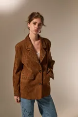 Blazer de gamuza color marrón con cuello solapa, corte holgado y detalle de tachas metálicas en solapas, bolsillos delanteros y puños.