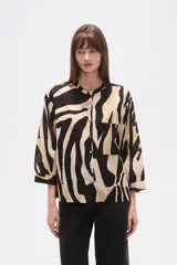 Camisa de corte holgado con estampado animal print tipo cebra en tonos negro y beige. Presenta cuello mao, cierre frontal con botones y un bolsillo aplicado en el pecho.