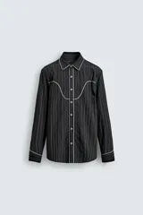 Camisa de corte relajado en color negro con rayas verticales finas. Presenta un diseño estilo western con vivos blancos en contraste en el canesú, cuello, tapeta frontal y puños. Cuenta con cuello solapa, cierre frontal de botones y mangas largas.