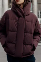 Campera puffer acolchada de color negro, con cuello envolvente, capucha integrada, manga larga, bolsillos laterales ocultos y bajo con elástico. Cierre frontal con botones a presión ocultos por solapa.