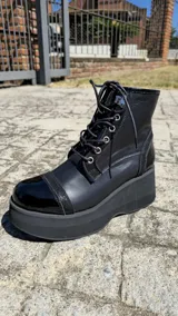 Borcego de cuero negro con plataforma alta y suela track. Cuenta con cordones frontales, ojetes metálicos y puntera de charol.