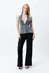 Pantalón de denim negro con corte wide leg, ruedo desflecado y detalle de tachas metálicas a lo largo de las costuras laterales.