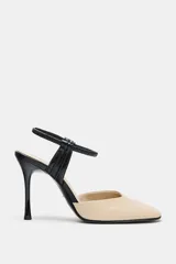 Zapato de tacón alto destalonado, fabricado en piel combinada en tonos beige y negro. Presenta punta redonda, tacón fino de 10 cm y tira elástica ajustable en el talón.