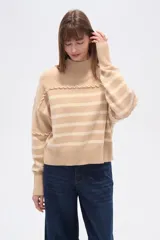 Sweater de punto color beige con rayas horizontales color crema, cuello alto y corte holgado. Presenta costuras decorativas en hombros y pecho.