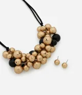 Conjunto de bijouterie compuesto por un collar con cordón negro ajustable y dije de esferas en tonos dorado y negro, acompañado por un par de aros tipo botón en tono dorado.