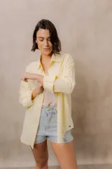 Camisa blanca de calce amplio, confeccionada en tejido liviano con sutiles rayas verticales, cuello clásico, mangas largas con hombros caídos y abotonadura frontal.