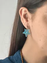 Aro tipo argolla con dije en forma de estrella de color celeste, decorado con cristales brillantes incrustados. El dije está pintado a mano y cuenta con un gancho de acero quirúrgico.