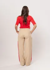 Pantalón beige de tiro alto con bolsillos delanteros y traseros, cierre frontal con cremallera y botón, y detalle de pespuntes rojos en los laterales.