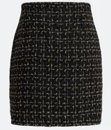 Pollera corta de tweed texturizado en color negro con hilos dorados, presenta botones decorativos con centro blanco y una pequeña abertura frontal en el ruedo.