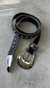 Cinturón negro de cuero sintético con hebilla metálica plateada estilo western y apliques de estrellas plateadas.