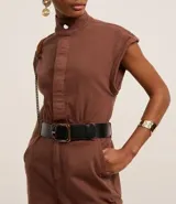 Mono largo de sarga color marrón, con cuello alto, cierre frontal con botones ocultos, sin mangas y bolsillos laterales. Incluye trabillas para cinturón.